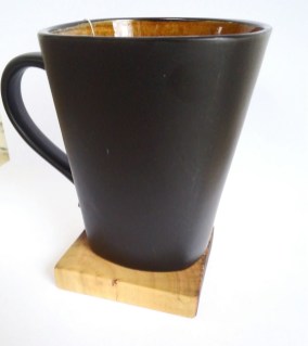 dark brown coffee mug sitting on wooden coaster with white background