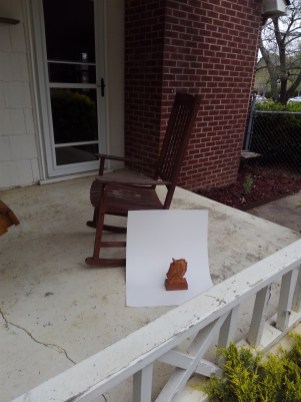 example of how to photograph small wood carving with a piece of white poster board taped to a rocking chair on an outdoor porch. Hand carved horse head sculpture is the subject being photographed