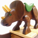 hand carved wooden triceratops dinosaur rocking toy. The dino is carved from walnut wood, left natural with oil finish. Poplar hand carved horns. It has a green painted wood saddle and leather handle. Green reptile eyes. Walnut rockers with maple slats. Small, size for 1-2 years old.