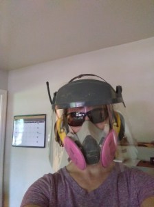 woman wearing dust respirator, ear protection, face shield, and sunglasses to protect face during power wood carving